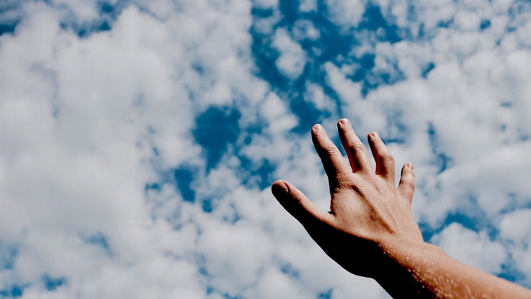 a hand holding a blue cloudy sky