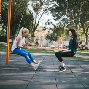 two girls sitting on swings in a park chatting